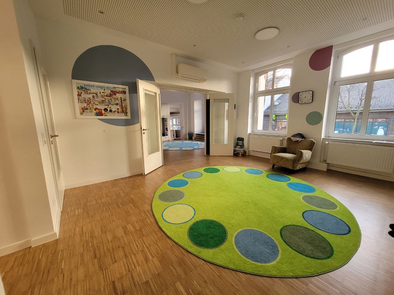 Heller Raum mit einem großen, runden, bunten Teppich und gemütlicher Sitzecke.