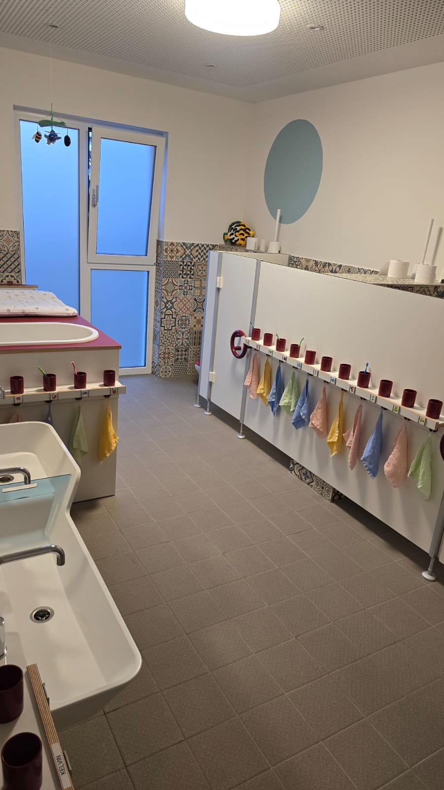 Blick in einen hellen Raum mit Waschbecken und farbigen Bechern an einer Wand.