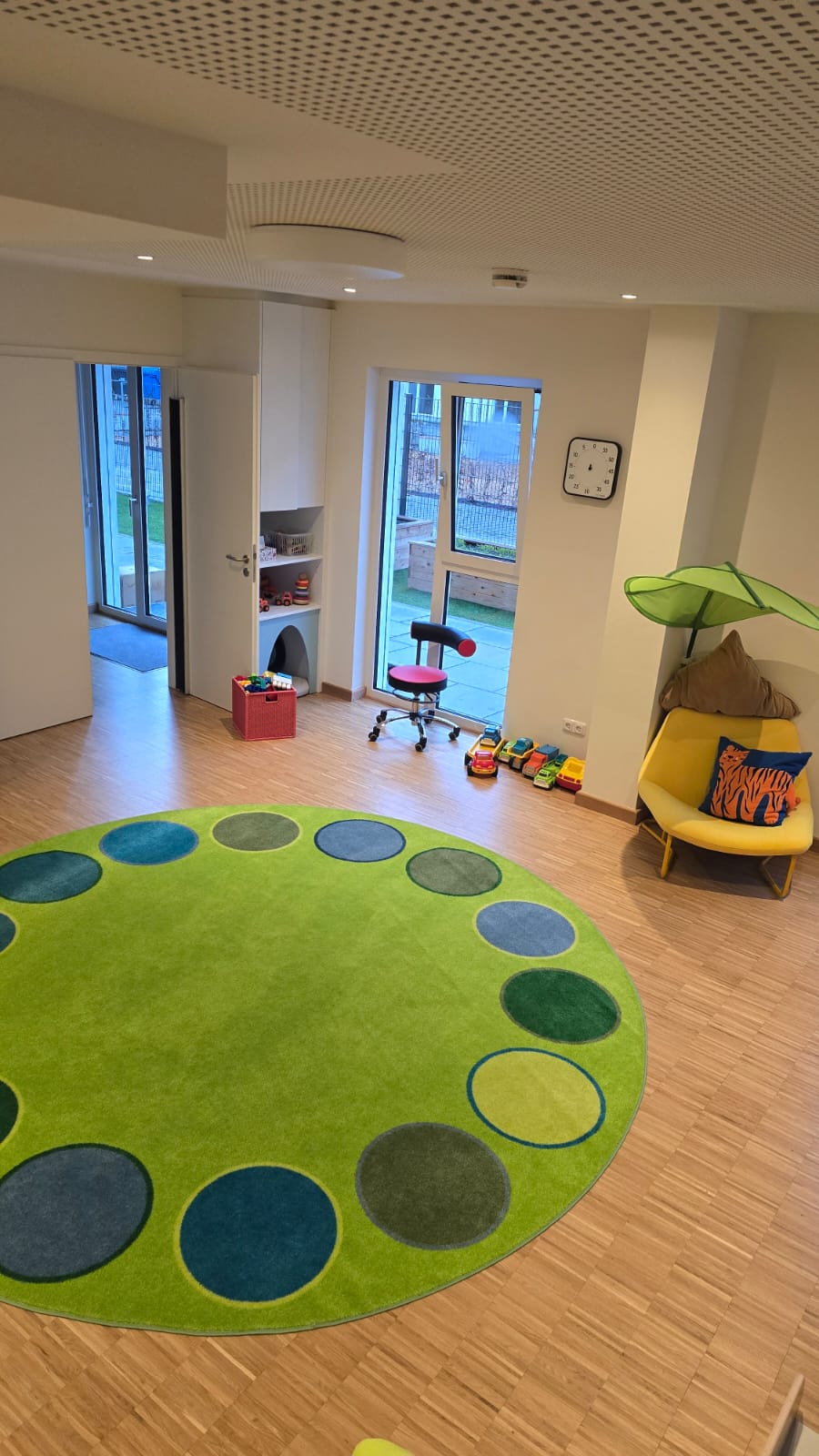 Bunte Spielmatte in einem hellen Raum mit Spielzeug und Möbeln für Kinder.