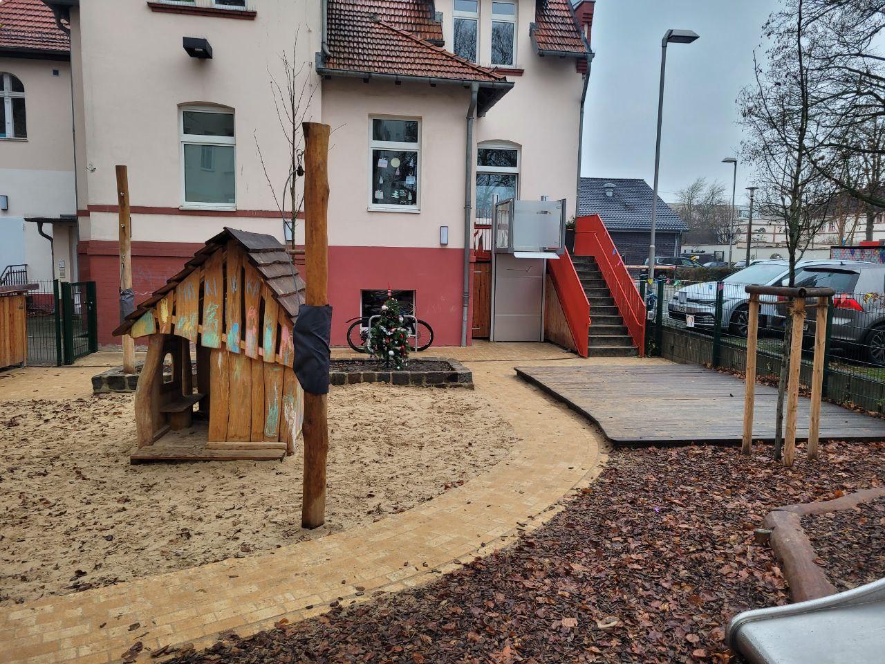 Spielplatz mit Holzstruktur, Rutsche und Wege aus Holz und Kieselsteinen.