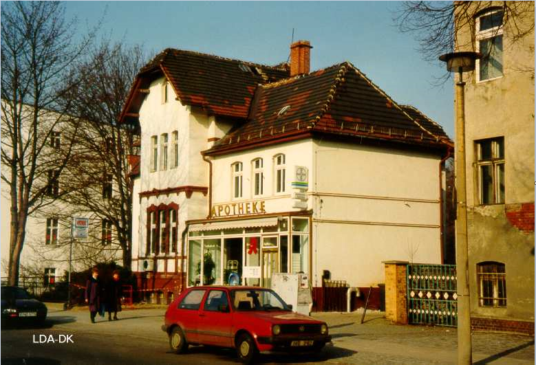 Rotes Auto vor einem historischen Gebäude mit weißer Fassade und braunen Fensterrahmen.
