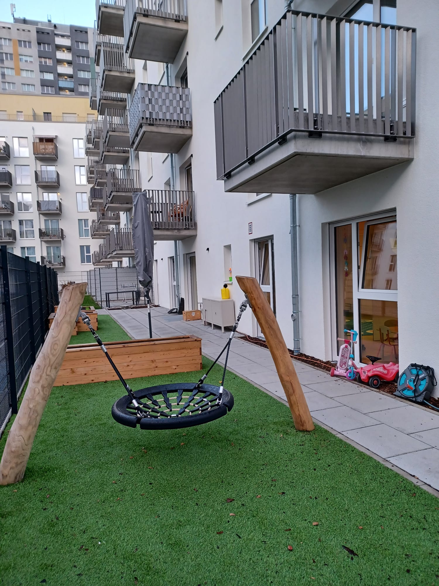 Schaukel im Gartenbereich eines Wohnhauses mit Rasen und Spielzeug im Hintergrund.