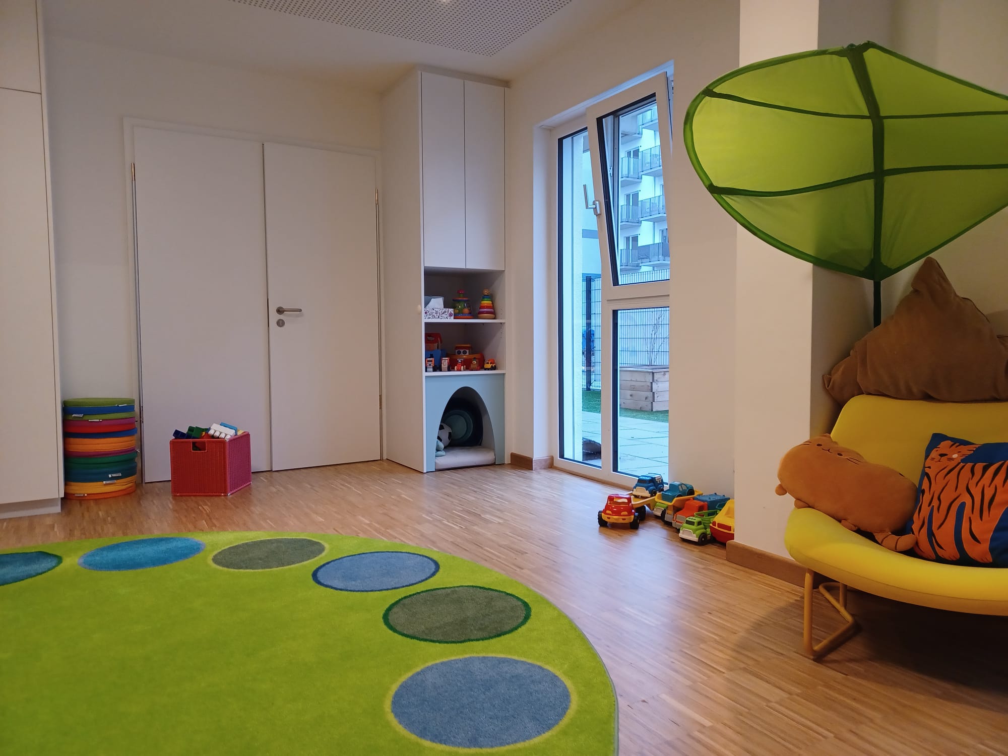 Bunter Spielbereich mit runder Teppichflächeund Regalen für Spielzeug.