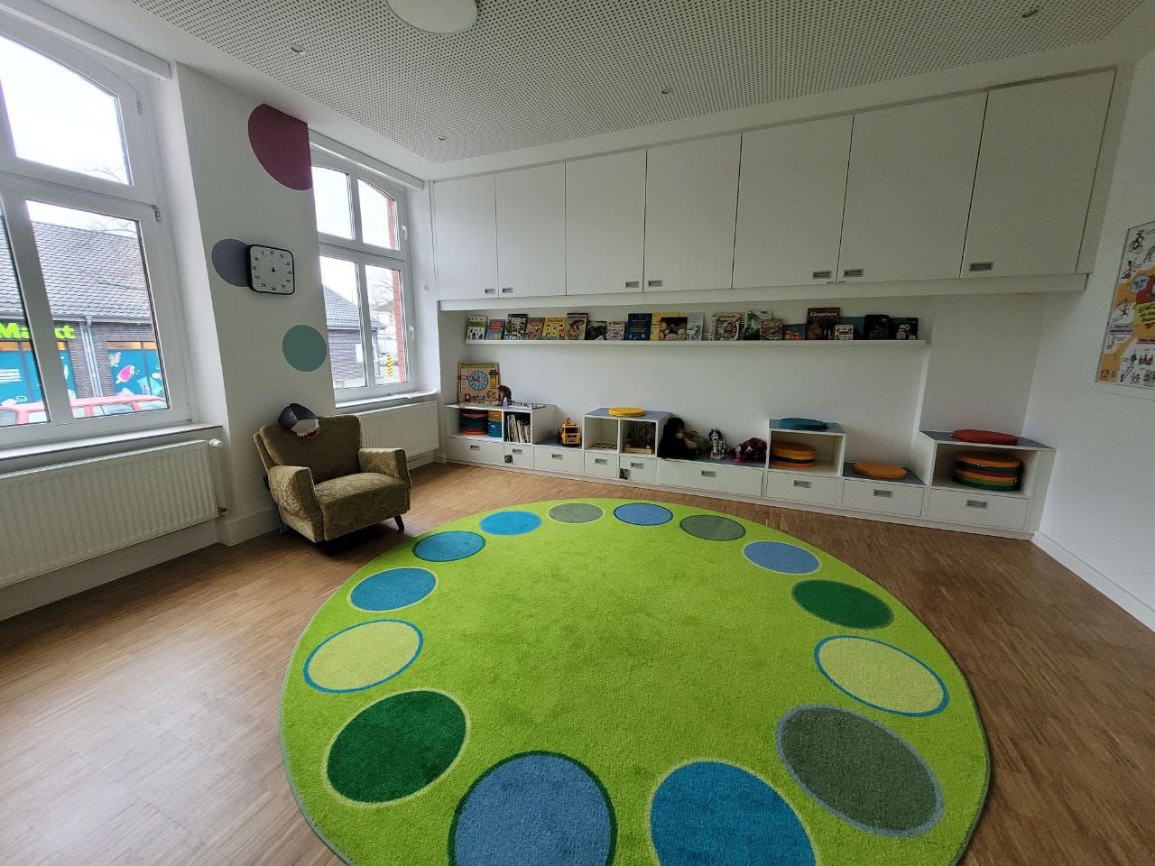 Ein heller Raum mit einem runden Teppich und Regalen voller Spielzeug.