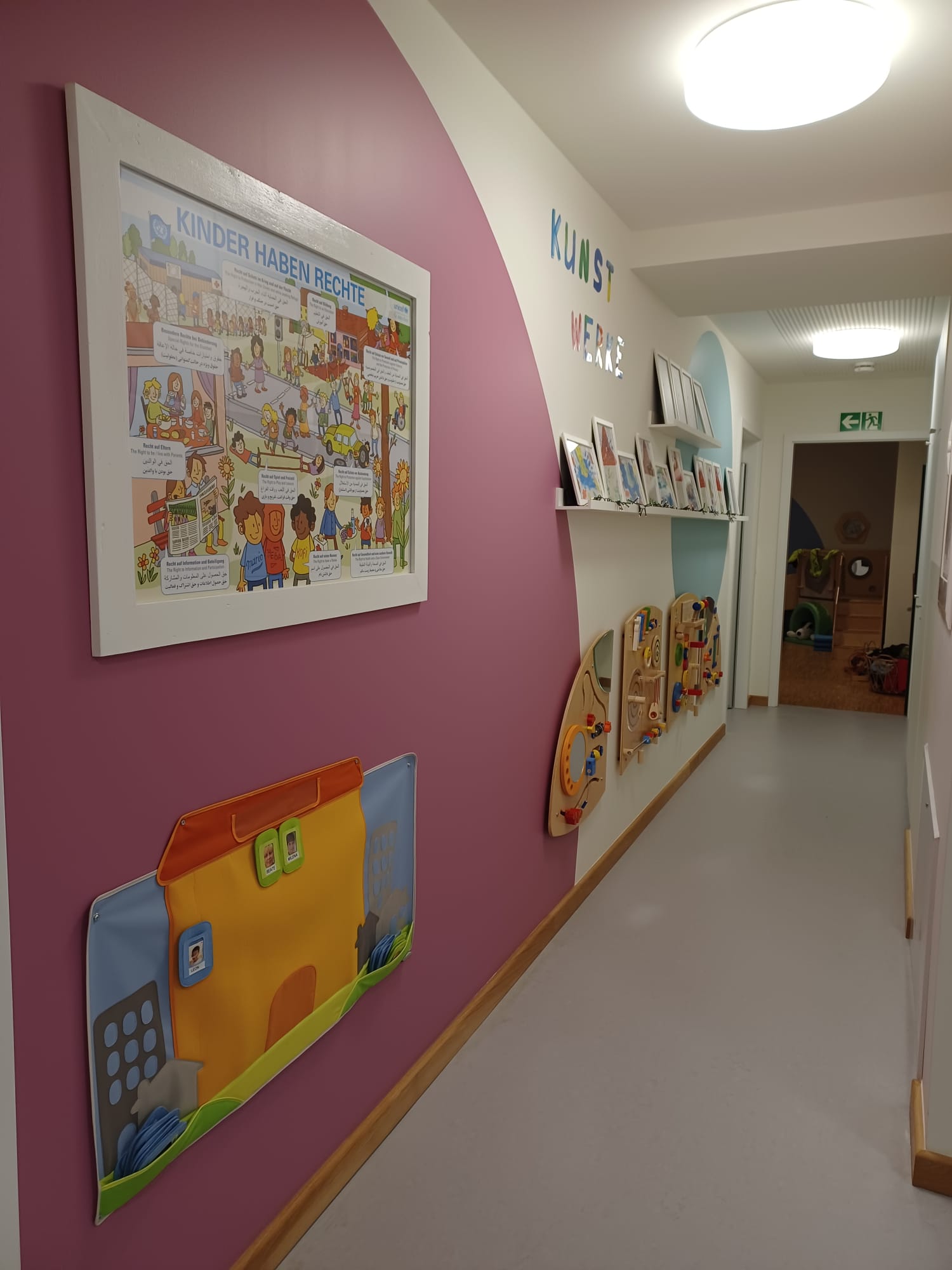 Bunter Flur mit Bilderrahmen, Spielzeugregalen und einer pinken Wand.