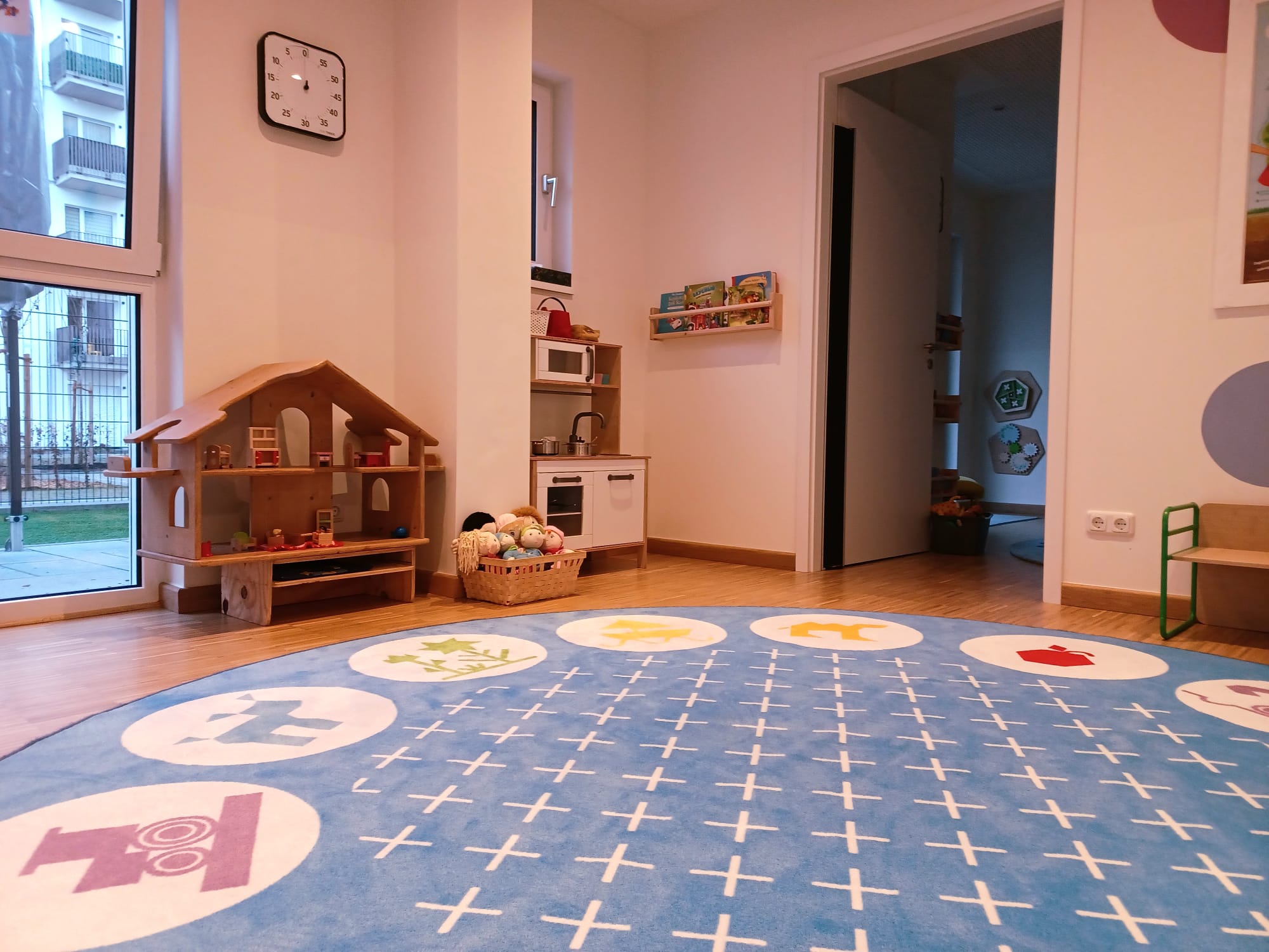 Spielzimmer mit Teppich, Spielzeughaus und Küchenzeile, Tageslicht von einem Fenster.