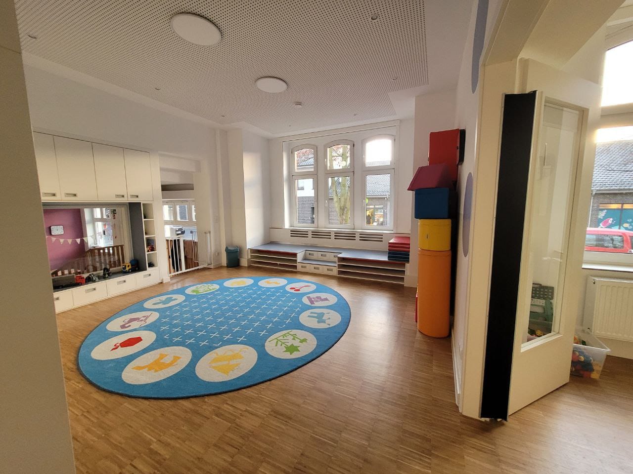 Heller Spielraum mit buntem Teppich, Fenstern und Sitzgelegenheiten.